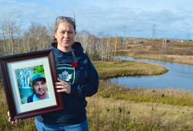 Amy Gerrow of Millville stands on the Alder Point Road in Bras d’Or, holding a picture of her brother, the late Jeff Harrietha, whose body was found in a lightly wooded area about 400-500 metres in back of her, on Sept. 10, 2020. Gerrow said her brother had rolled his ATV and was trapped under it and had placed a call to 911, however says police were negligent in treating the call as a hoax and six days later he was found dead. Sharon Montgomery-Dupe/Cape Breton Post