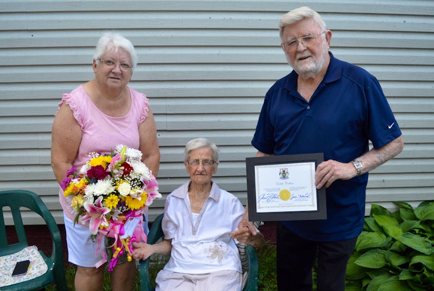Edith Collins, centre, became Cape Breton's latest centenarian when she turned 100 on Thursday. While she said she just wanted a quiet day, she spent much of it in the garden of her Whitney Pier home welcoming well-wishers who popped by to congratulation her on her milestone birthday. Daughter Patricia, left, holds a bouquet of flowers that Cape Breton Regional Municipality Coun. Jim MacLeod, right, brought by on behalf of the municipality. Collins was born in Newfoundland but spent most of her life in Sydney. DAVID JALA/CAPE BRETON POST
