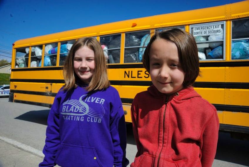 Kaitlyn Coade, left, and Antonio Perez Diaz, both Grade 3 students at C.C. Loughlin Elementary School in Corner Brook, pose for a photo by a school bus jam-packed with plastic bags their school collected during the month of May.