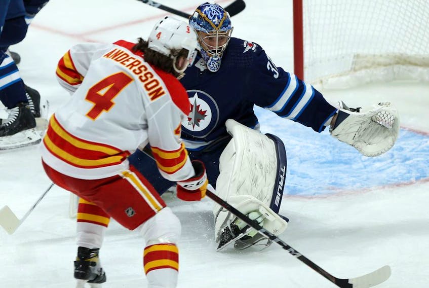 Winnipeg Jets goaltender Connor Hellebuyck is at the mercy of Calgary Flames defenceman Rasmus Andersson during NHL action in Winnipeg on Jan. 14, 2021. 