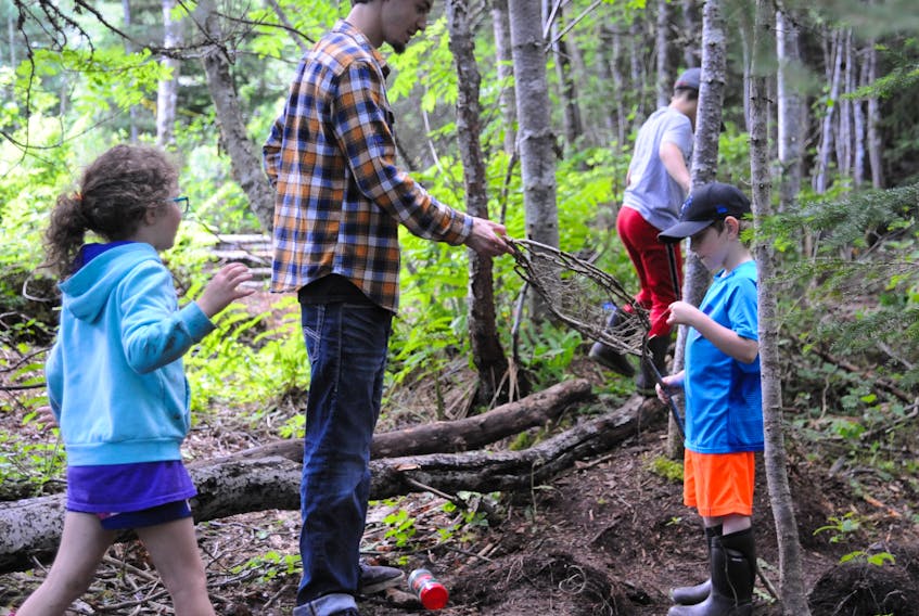 Assistant instructor Ken Barry assists six-year-old Paul Robertson with making a basket out of twigs and branches during the Forest Day Camp being held this week at the Blow-Me-Down Trails in Corner Brook. There will be another edition of the play-based kids camp organized by Sapling Forest School at the site next week and a larger one at the Grenfell Campus site later this summer. Coming to check on the project's progress is Katherine Mackey, 6, while Brody Hicks, 7, carefully walks along some fallen logs in the background.
