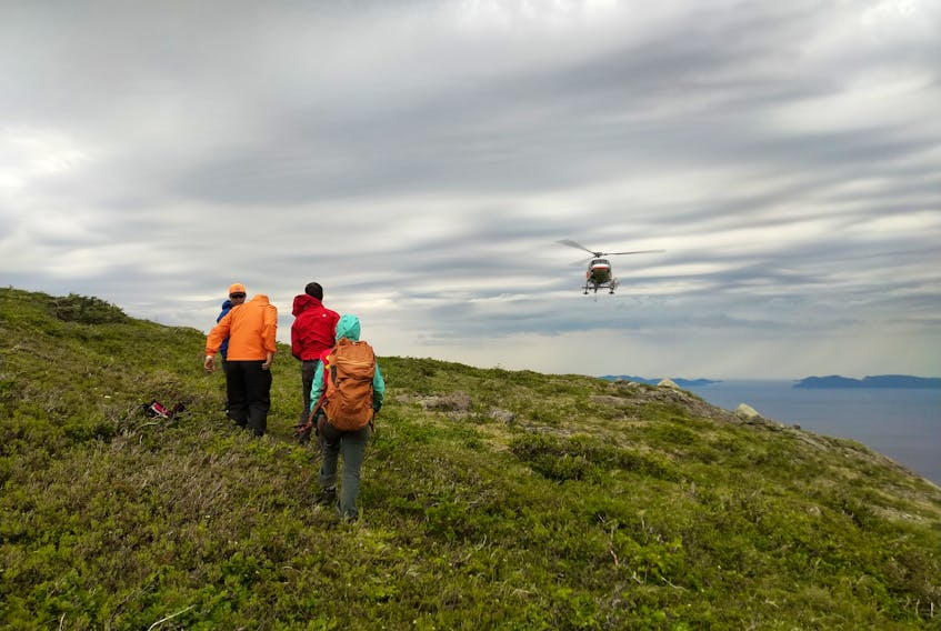 Two members of the Bay of Islands Search and Rescue Team stand with the two hikers they rescued await an incoming helicopter to fly them out from Blow Me Down Mountain where they got lost.
