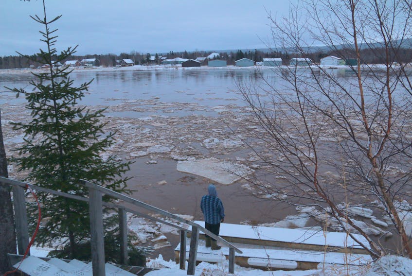 A man stands on a wharf, watching the high water levels and ice pans and slob drifting down the Humber River Sunday.