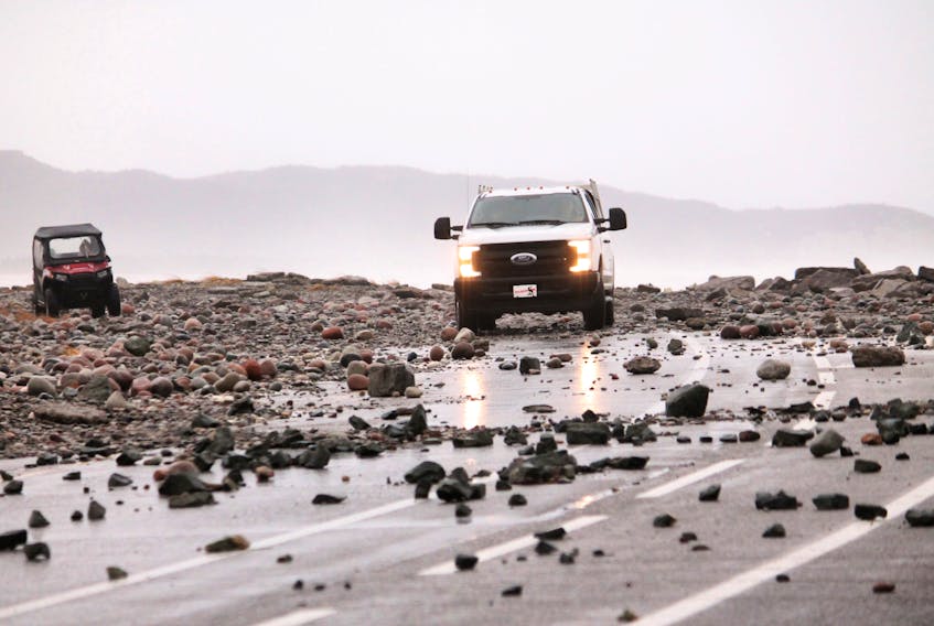 A side-by-side and a pickup truck are seen making their way over beach rocks strewn across Massachusetts Drive on the road leading to Little Port Harmon.