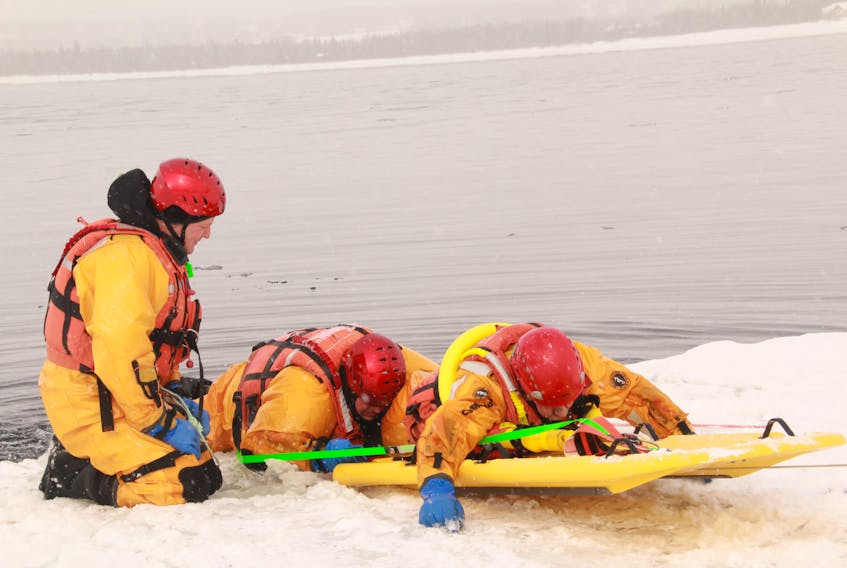Grant Curnew watches as Deer Lake search and rescue members Darren Williams and Wayne Anstey use the ice rescue board in the frigid waters of Deer Lake.