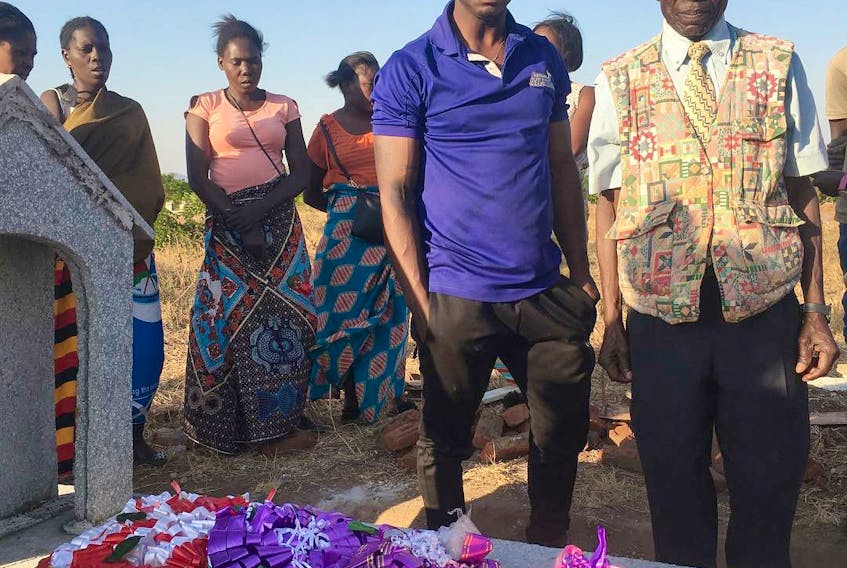 Jules Ohelo stands at the grave of his uncle during his recent return trip to Africa.