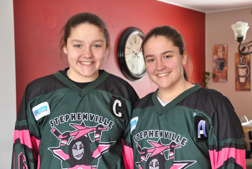 Cathy Morgan, left and twin sister Abby pose for a photo together in Stephenville Thursday afternoon. The twin sisters will be gunning for gold today as members of the host team for the provincial U15 female A hockey tournament being held this weekend at the Stephenville Dome.
