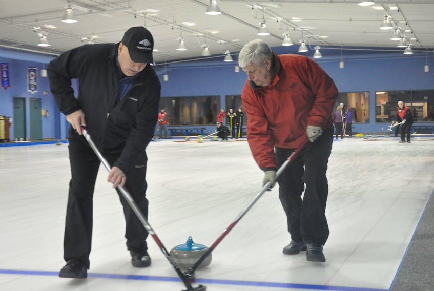 Jim Conway, left, and Derek Hamlyn work with their brooms to get their team’s rock to maintain a straight path towards the house during Commercial League play at the Corner Brook Curling Club on Wednesday night.