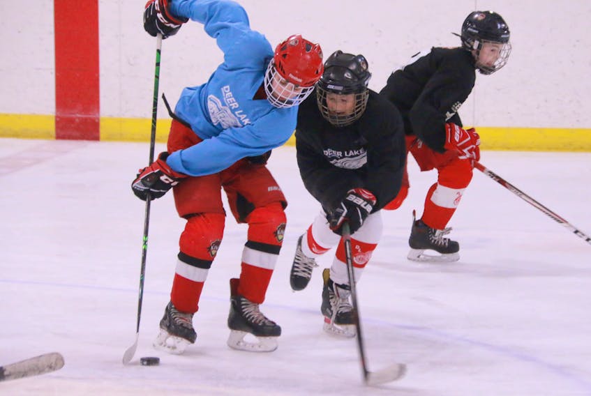 Here, in peewee division play, Team Blue’s Matthew Reid, left, and Team Black’s Ben Cornick reach for a loose puck as Team Black’s Lucas Payne skates ahead to get ready for a pass.
