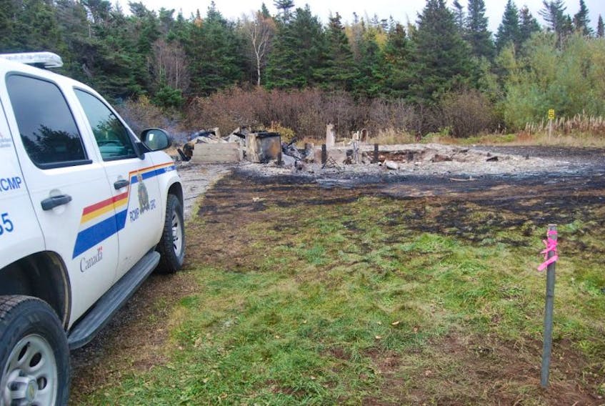 A police vehicle is seen parked next to a home destroyed by fire in Flat Bay East on Oct. 26, 2015.
