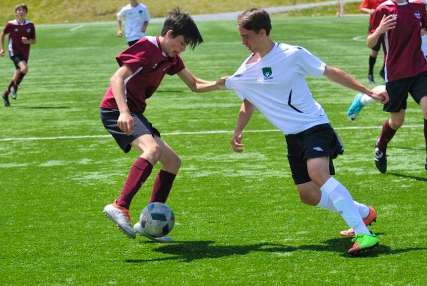 Taj Exley, left, of Team Newfoundland and Labrador grabs onto the jersey of Kyle Gould of Team New Brunswick s they battle for the ball in first-half action of their boys Under-14 Atlantic Soccer Championship round-robin match at the Wellington Street Complex in Corner Brook Thursday afternoon.