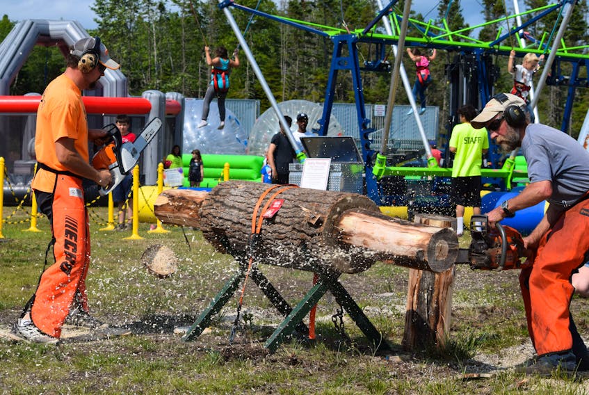 Sawdust flies as competitors go head to head in the chainsaw competition at the Barrington Municipal Exhibition, while children play on the rides in the background, making for a festive scene.