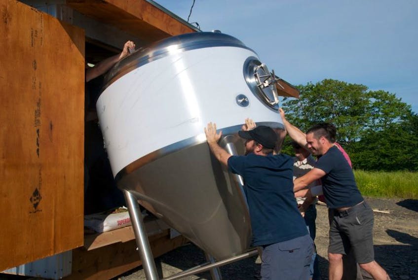 Les Barr (inside the shelter) and the gang angle the fermenter so it can fit inside its new brewpub home.