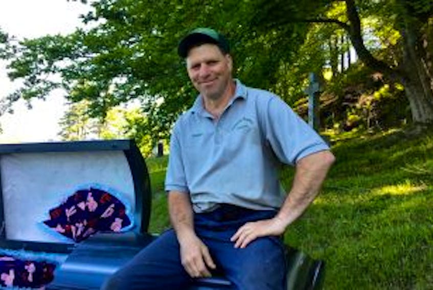 ['Tim MacKinnon has been a gravedigger at Yarmouth Mountain Cemetery for 22 years. One of his strangest episodes on the property involved a black cat. MacKinnon builds Halloween props in his spare time, including the comfortable coffin he’s sitting on.']