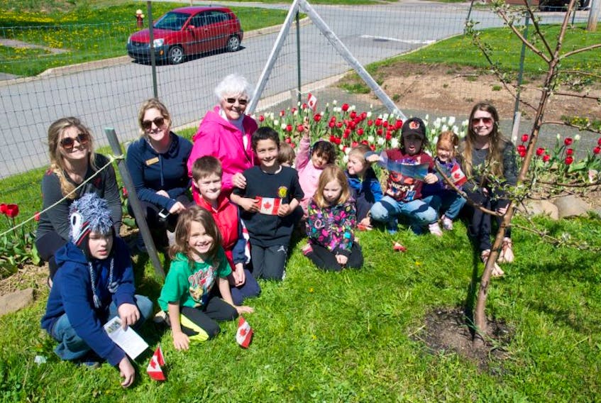 Elizabeth McMichael sits with kids from the YMCA After School Program and some program workers in front of the Canada 150 tulips, which were planted in the shape of the Canadian flag. “I don’t see much of a flag… but they’re still beautiful,” said McMichael.