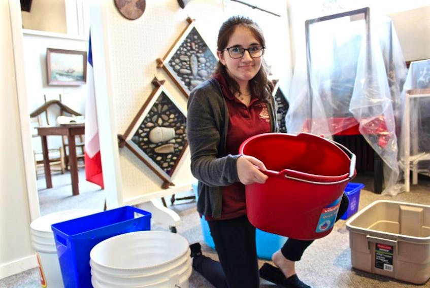 Summer student Meredith James with one of many buckets on hand for catching drips from a leaky roof at the Yarmouth County Museum & Archives. The museum is seeking donations towards the estimated $68,000 cost of repair.