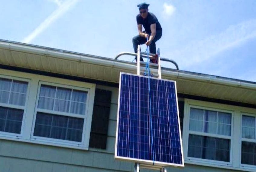 Chris Bird, owner of Rehome a company that will design and install a solar system, raises a solar panel to Sherman and Cindy Embrees roof last week.