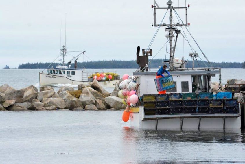 As lobster traps are unloaded onto the wharf from a boat dockside, another fishing vessel brings in a load of traps and gear prior to the end of the LFA 34 lobster season in Pinkney's Point, Yarmouth County.
